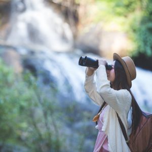 Female tourist who is looking at the binoculars to see the atmosphere at the waterfall